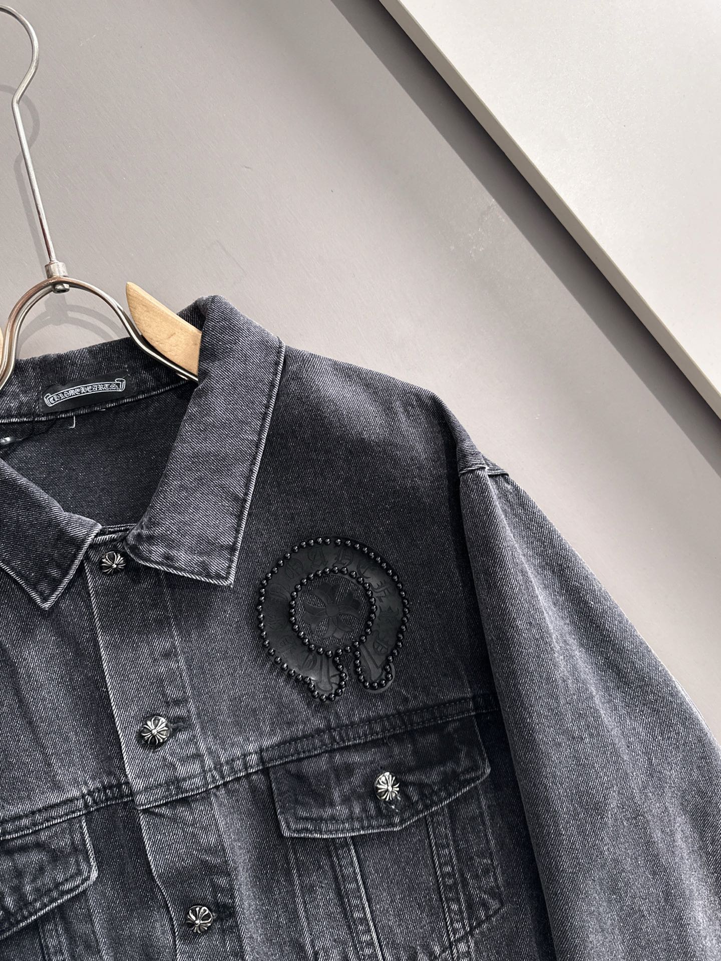 Dark denim jacket shoulder and sleeve detail with studded emblem on the chest
