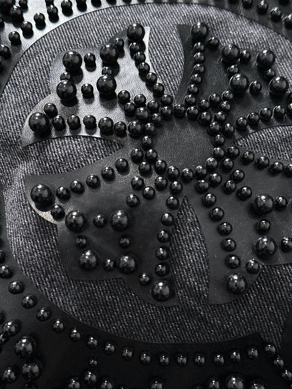 Large studded emblem close-up on denim, with raised beads forming an ornate pattern