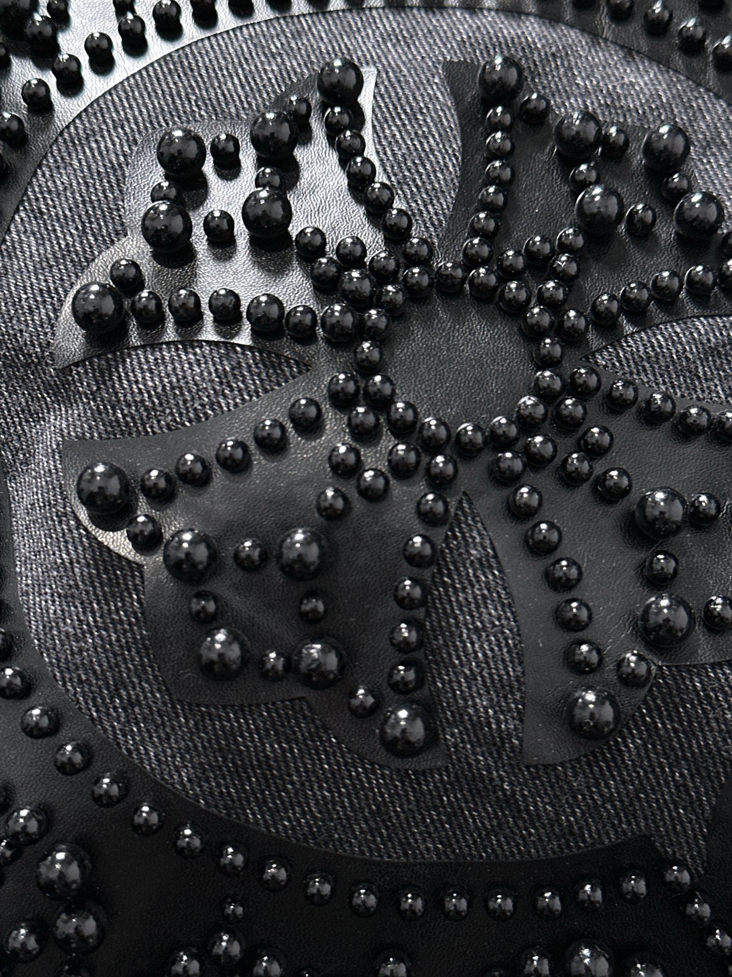 Large studded emblem close-up on denim, with raised beads forming an ornate pattern