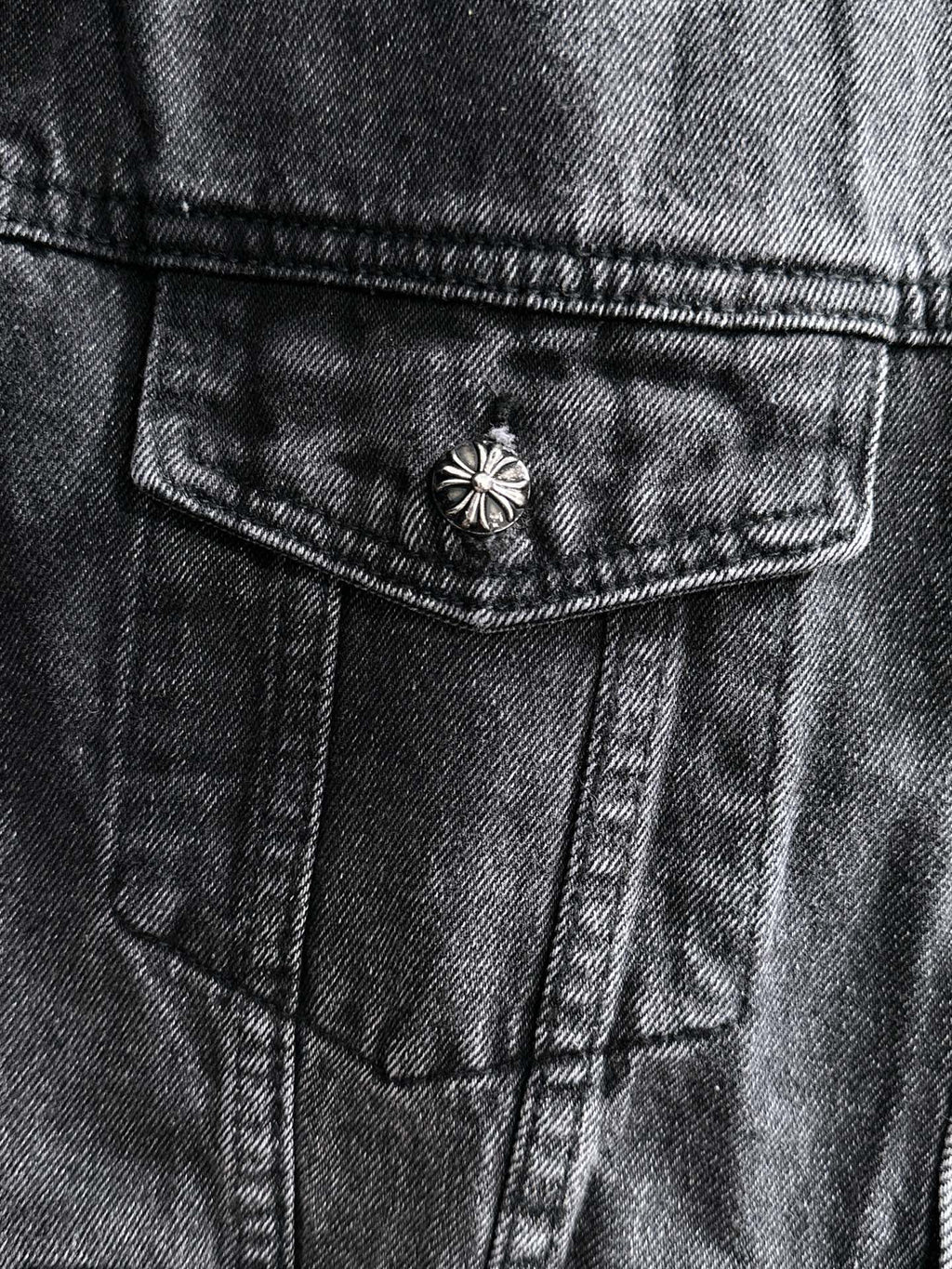 Dark denim jacket close-up of front pocket with small studded flower button detail
