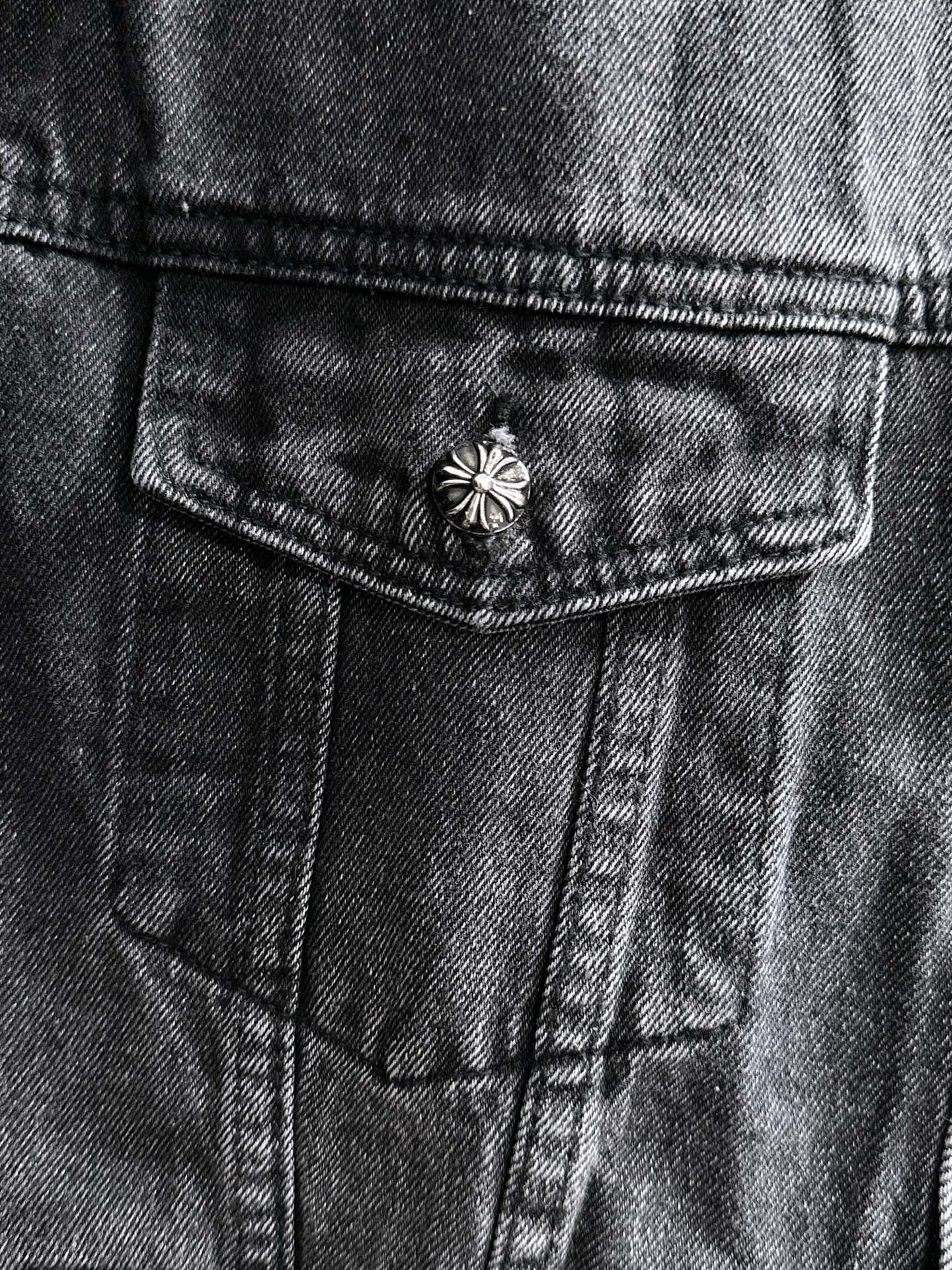 Dark denim jacket close-up of front pocket with small studded flower button detail