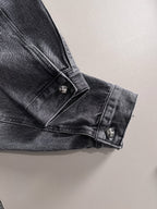 Dark denim jacket cuff close-up with button and small studded emblem