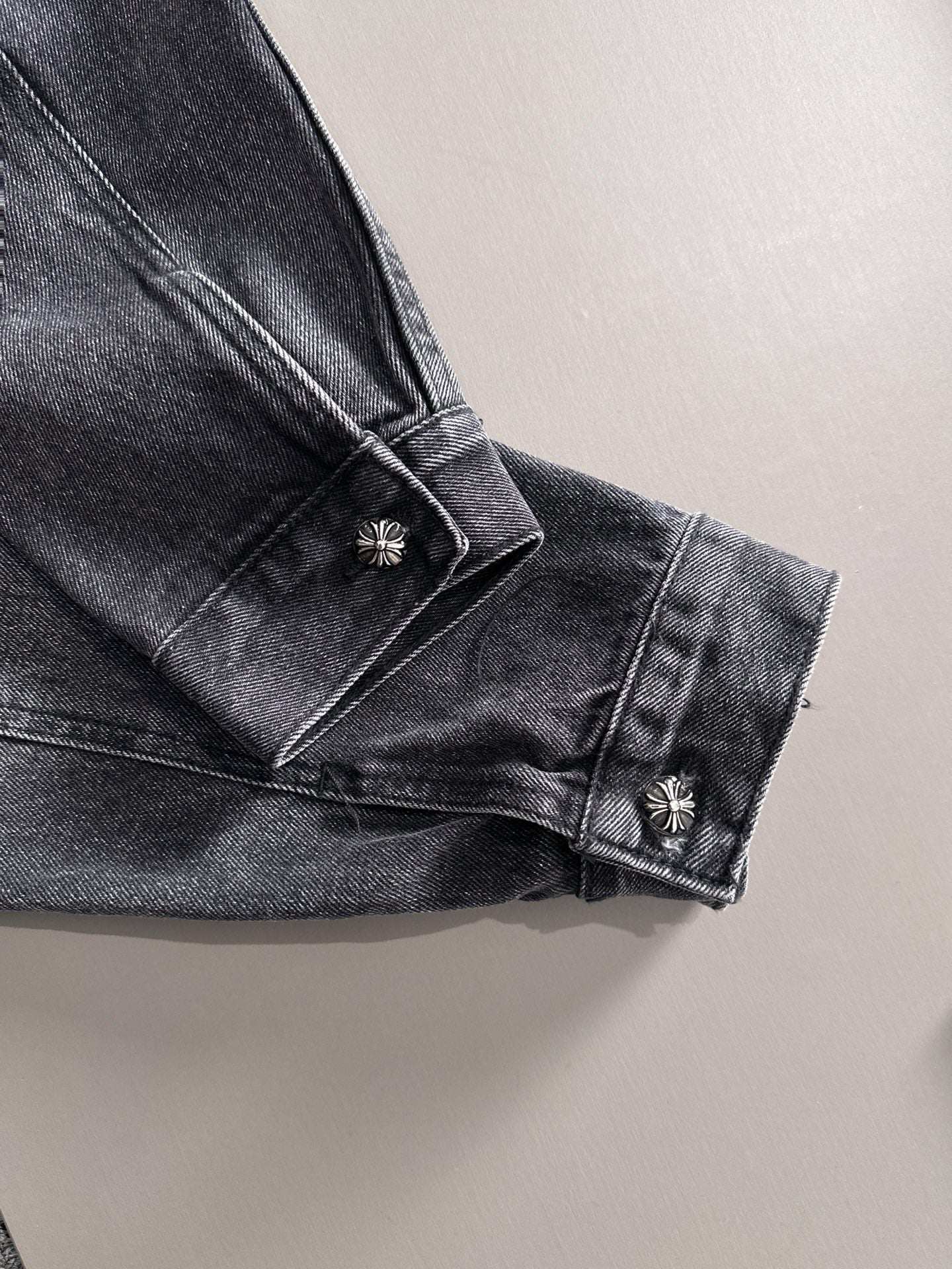 Dark denim jacket cuff close-up with button and small studded emblem