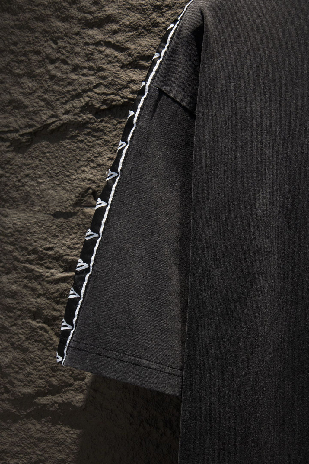 Balenciaga black T-shirt side view with white logo tape along sleeve edge
