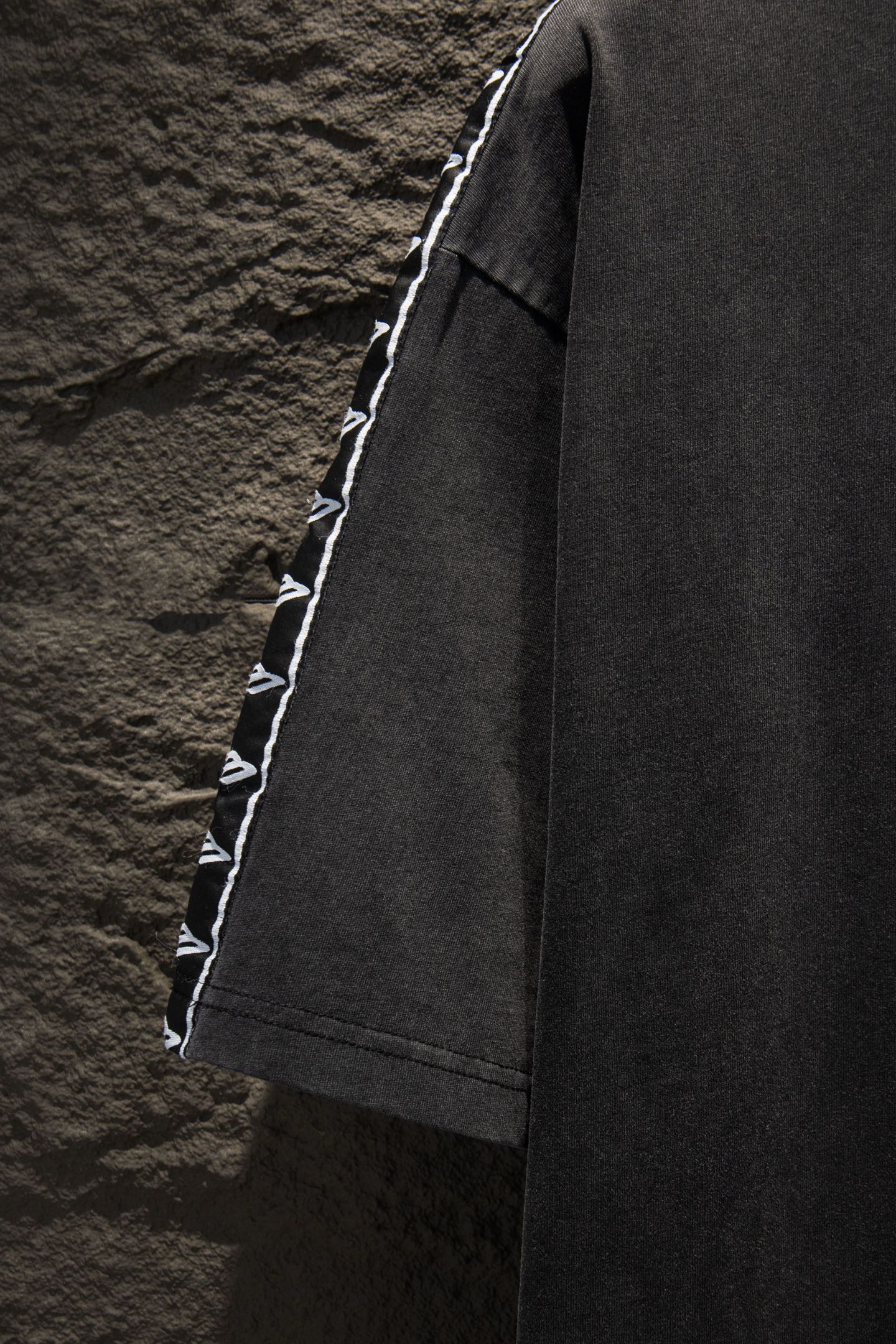 Balenciaga black T-shirt side view with white logo tape along sleeve edge