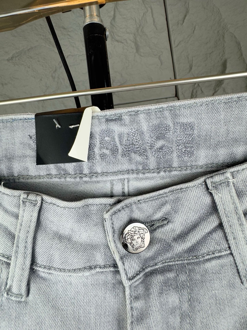 Light-wash denim jeans waistband close-up with round logo button and belt loops