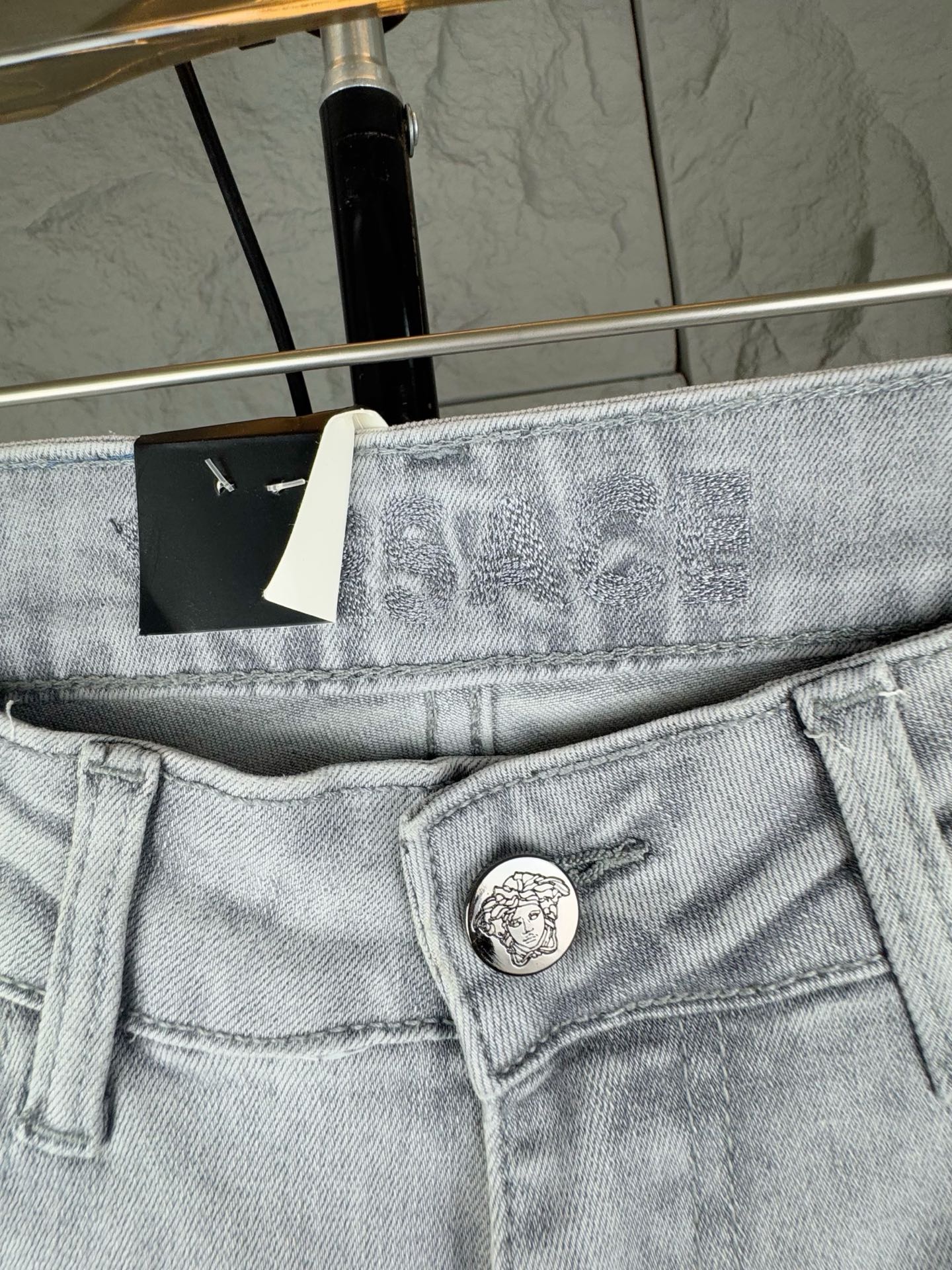 Light-wash denim jeans waistband close-up with round logo button and belt loops