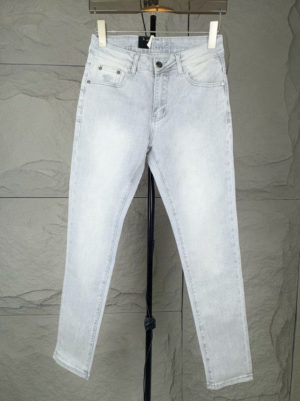 Light blue denim jeans on hangers, front view with belt loops and button closure