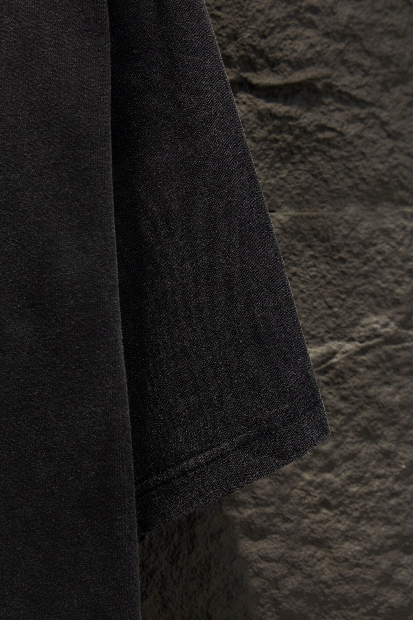 Black T-shirt sleeve and side seam view, hanging on wall