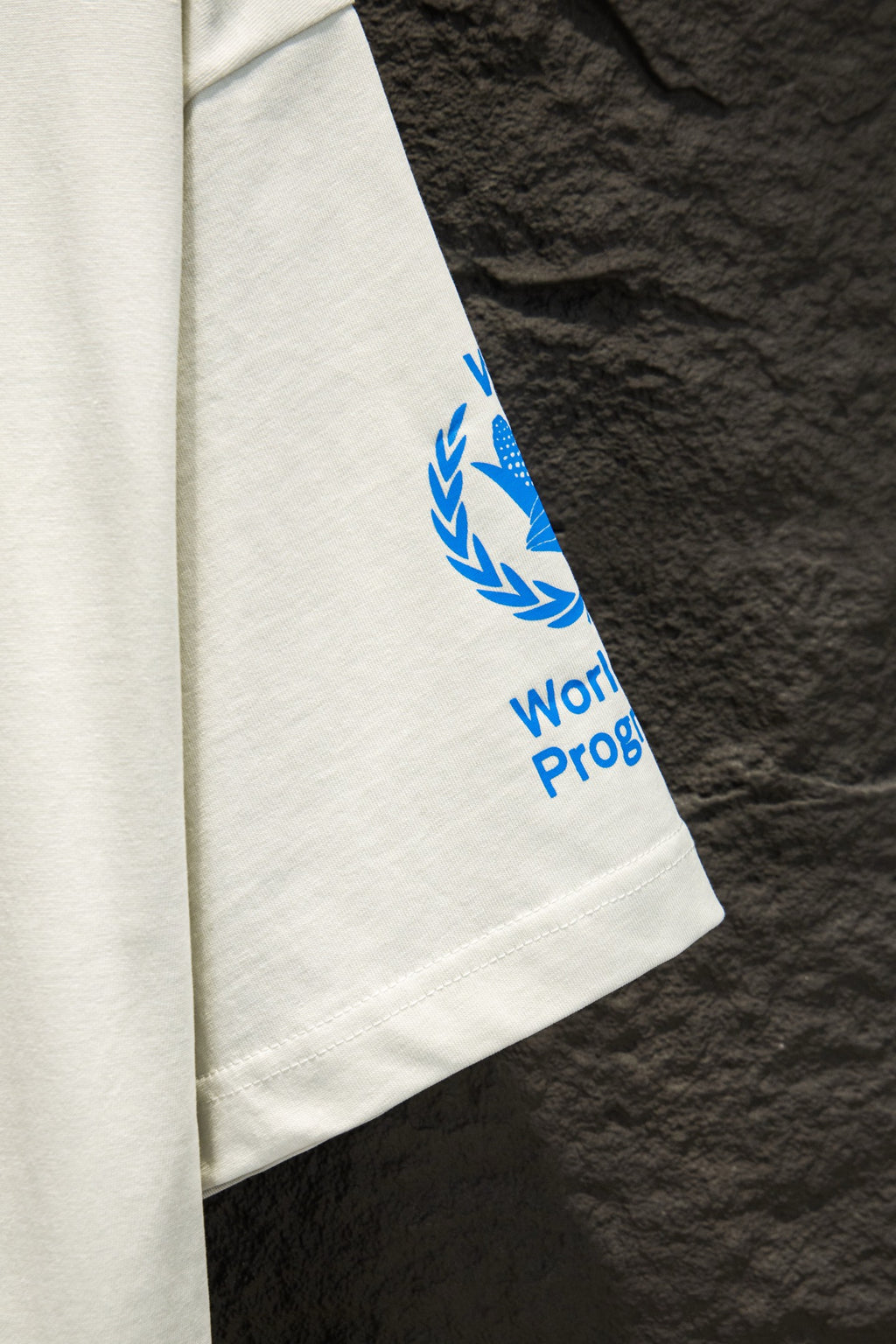 White T-shirt sleeve with blue WFP Proof graphic and laurel icon