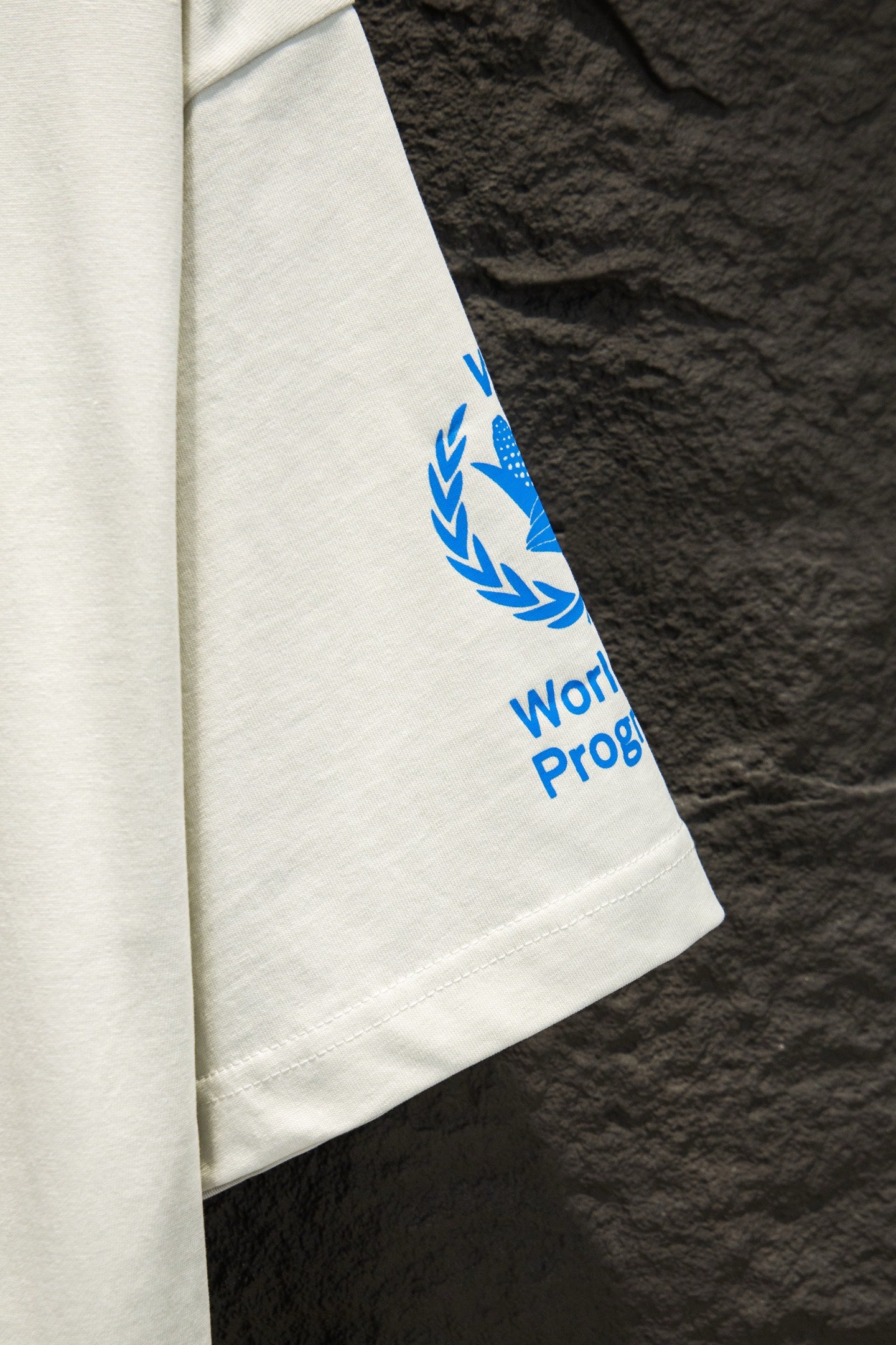 White T-shirt sleeve with blue WFP Proof graphic and laurel icon