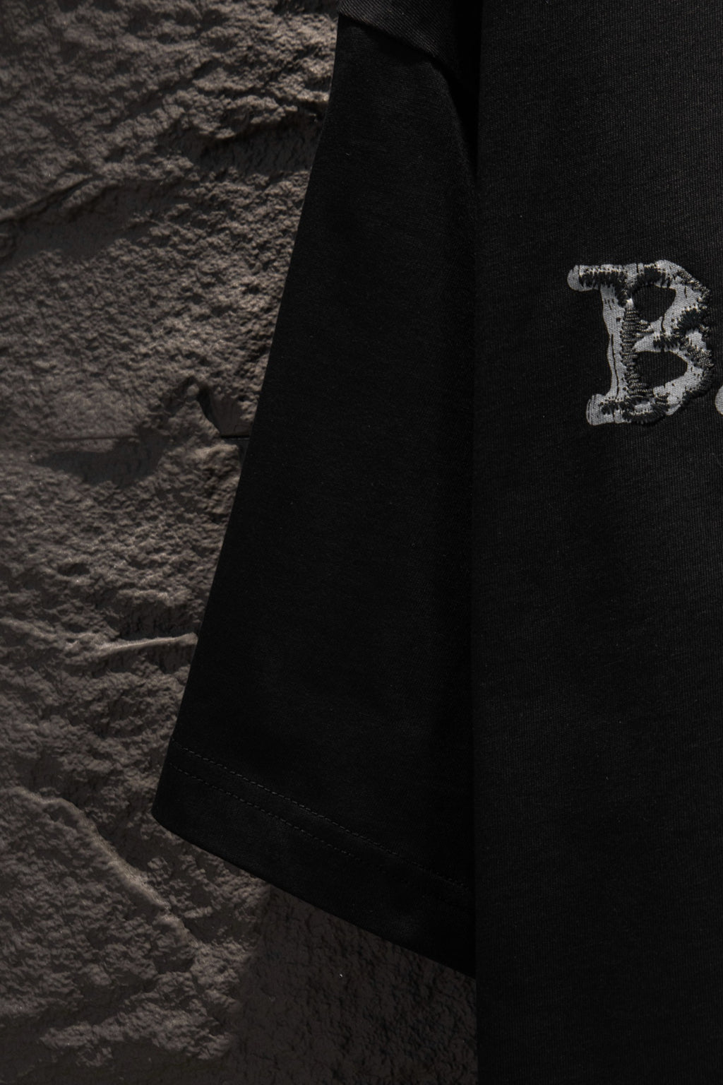 Black short-sleeve T-shirt with partial letter graphic near hem.