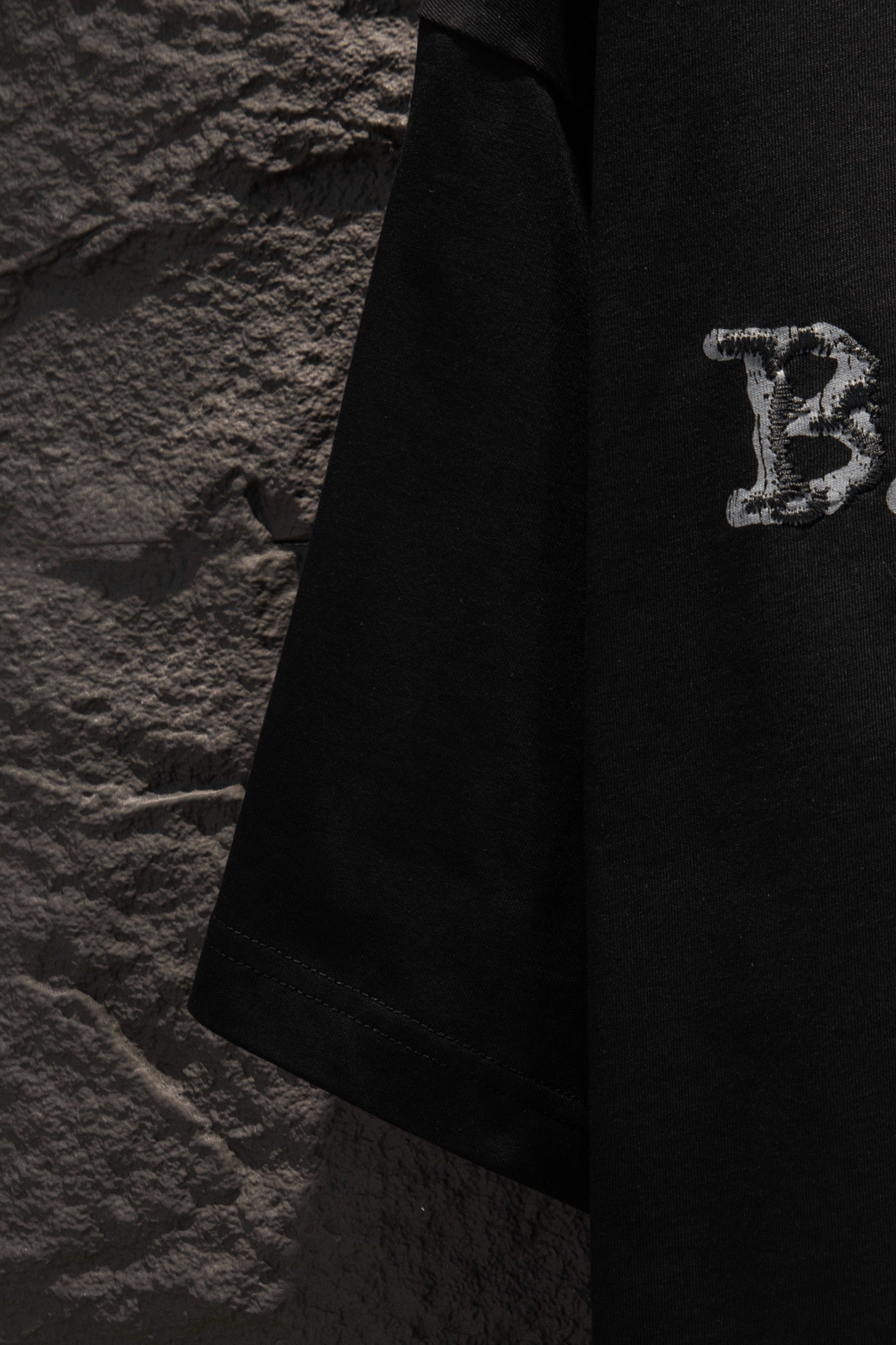Black short-sleeve T-shirt with partial letter graphic near hem.