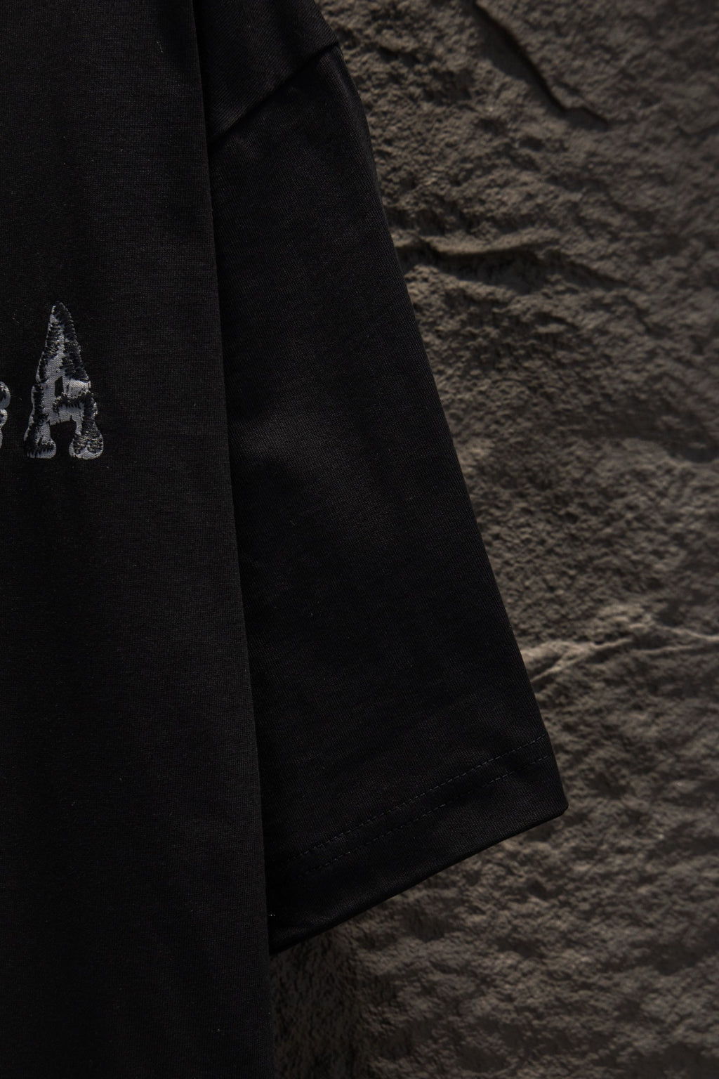 Black short-sleeve T-shirt with small letter graphic on sleeve.