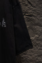 Black short-sleeve T-shirt with small letter graphic on sleeve.