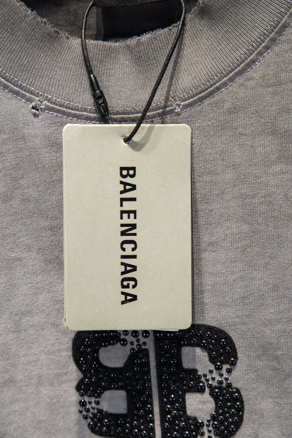 Light gray T-shirt neckline with hanging Balenciaga tag and studded logo