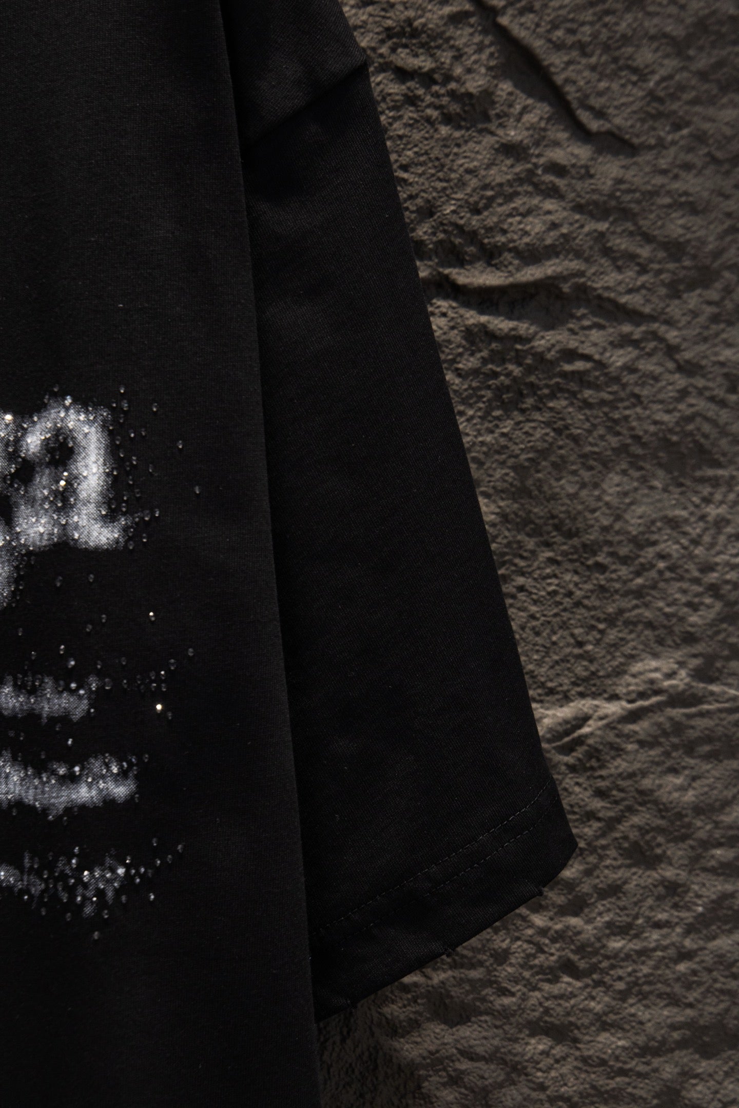 Black T-shirt close-up of sleeve and lower side with partial distressed print
