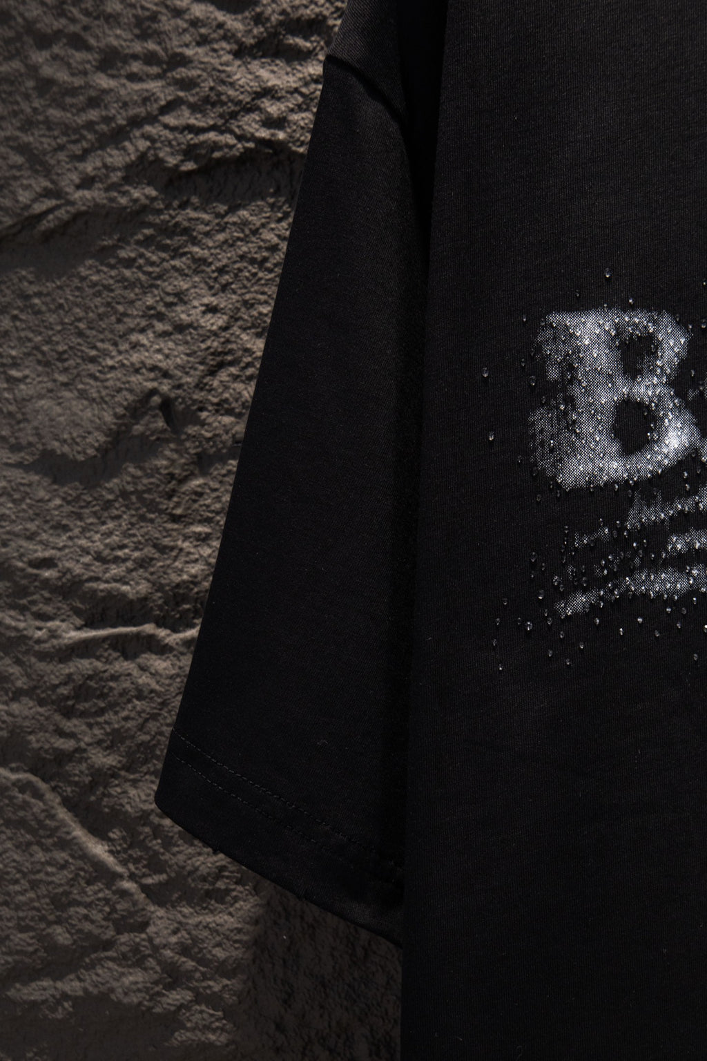 Black T-shirt side view with partial distressed logo print near the sleeve