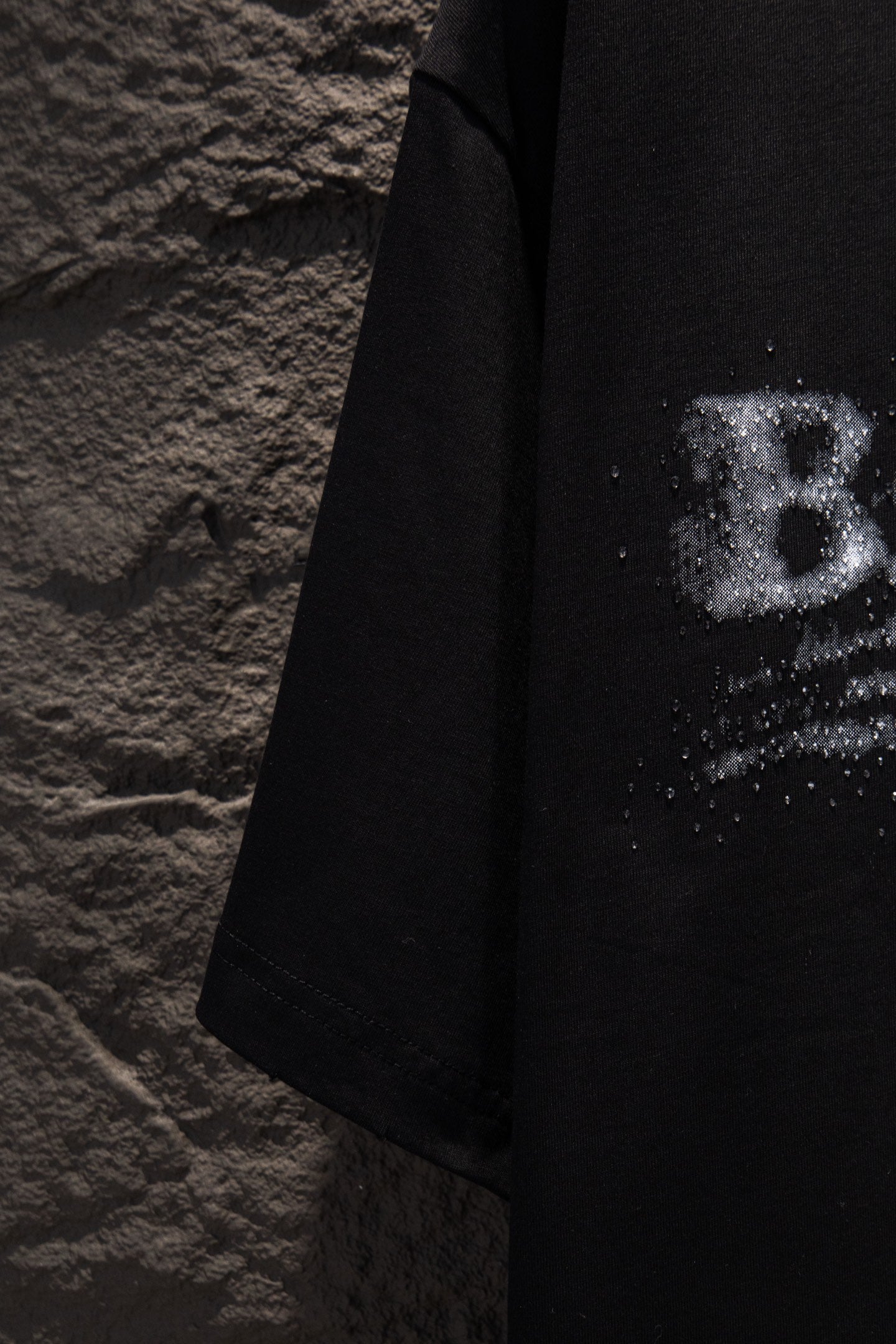 Black T-shirt side view with partial distressed logo print near the sleeve