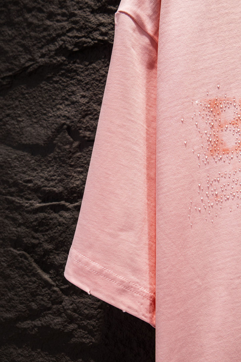 Pink T-shirt side seam and drape with rhinestone logo detail near chest
