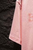 Pink T-shirt side seam and drape with rhinestone logo detail near chest