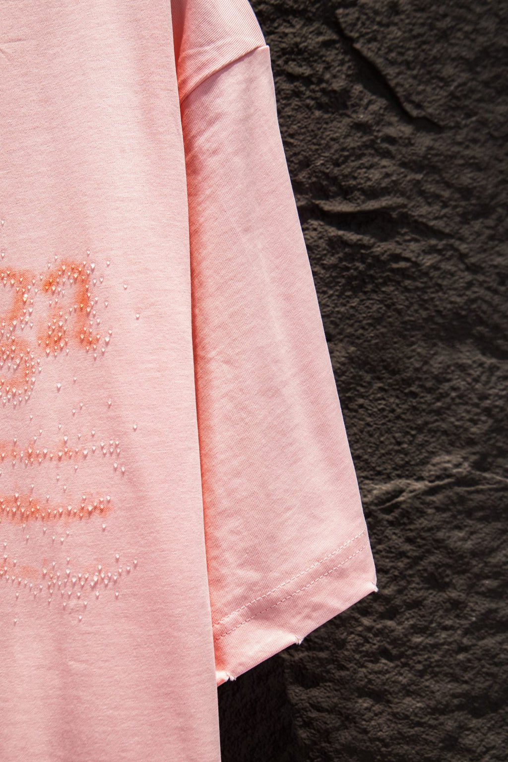 Pink T-shirt sleeve and side drape with rhinestone logo detail near hem