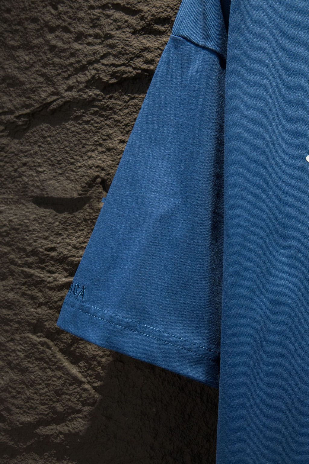 Blue T-shirt side view with curved hem and stitched sleeve cuff