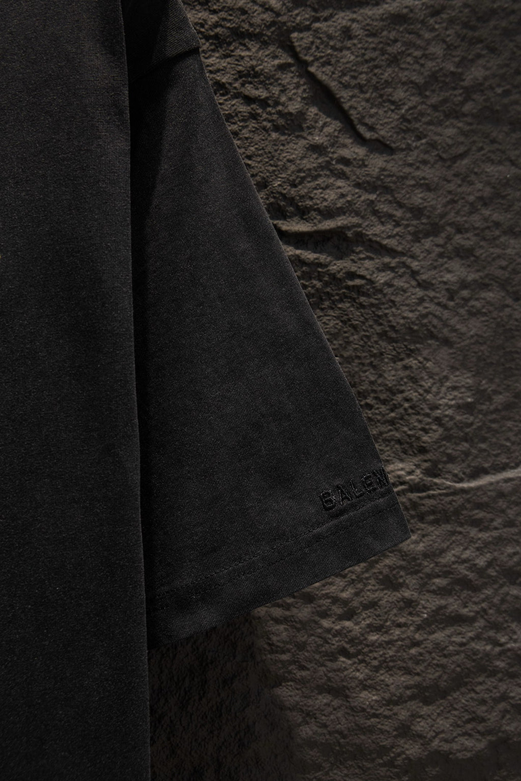 Black T-shirt sleeve with small “BALENCIAGA” embroidery near the hem