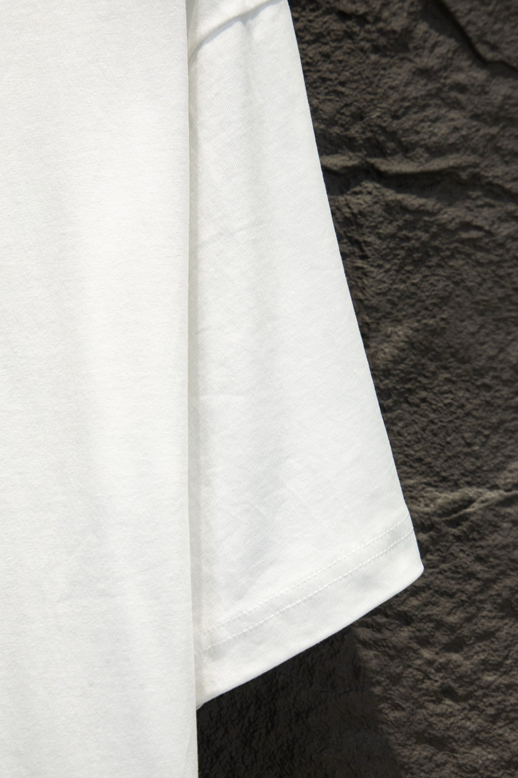 White short-sleeve T-shirt side view with straight hem and visible seam stitching.