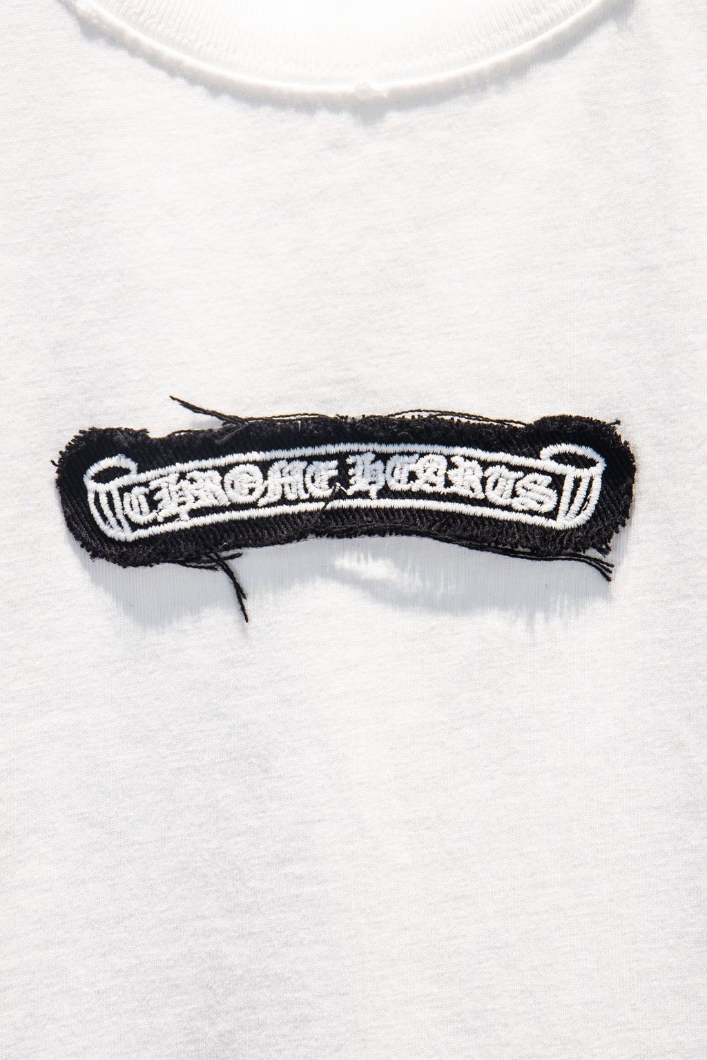 Black embroidered logo patch detail on white T-shirt chest