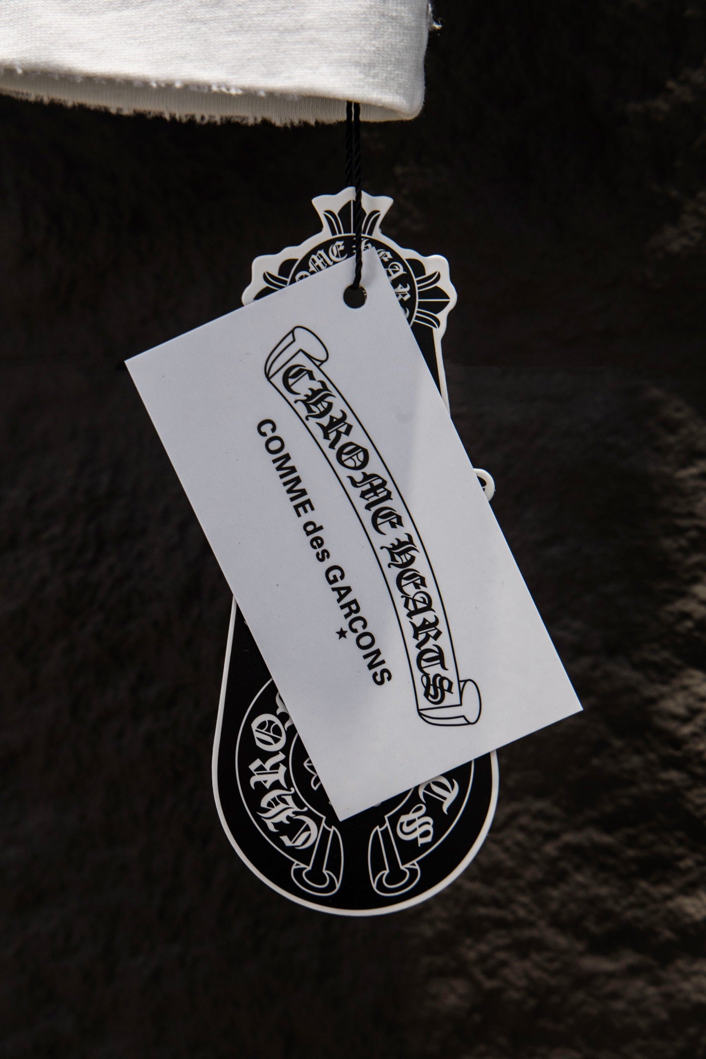 Garment tag reading Chrome Hearts and Combines Operations, hanging from T-shirt.