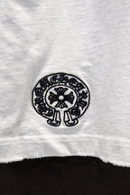 White T-shirt with small black circular emblem at lower hem.