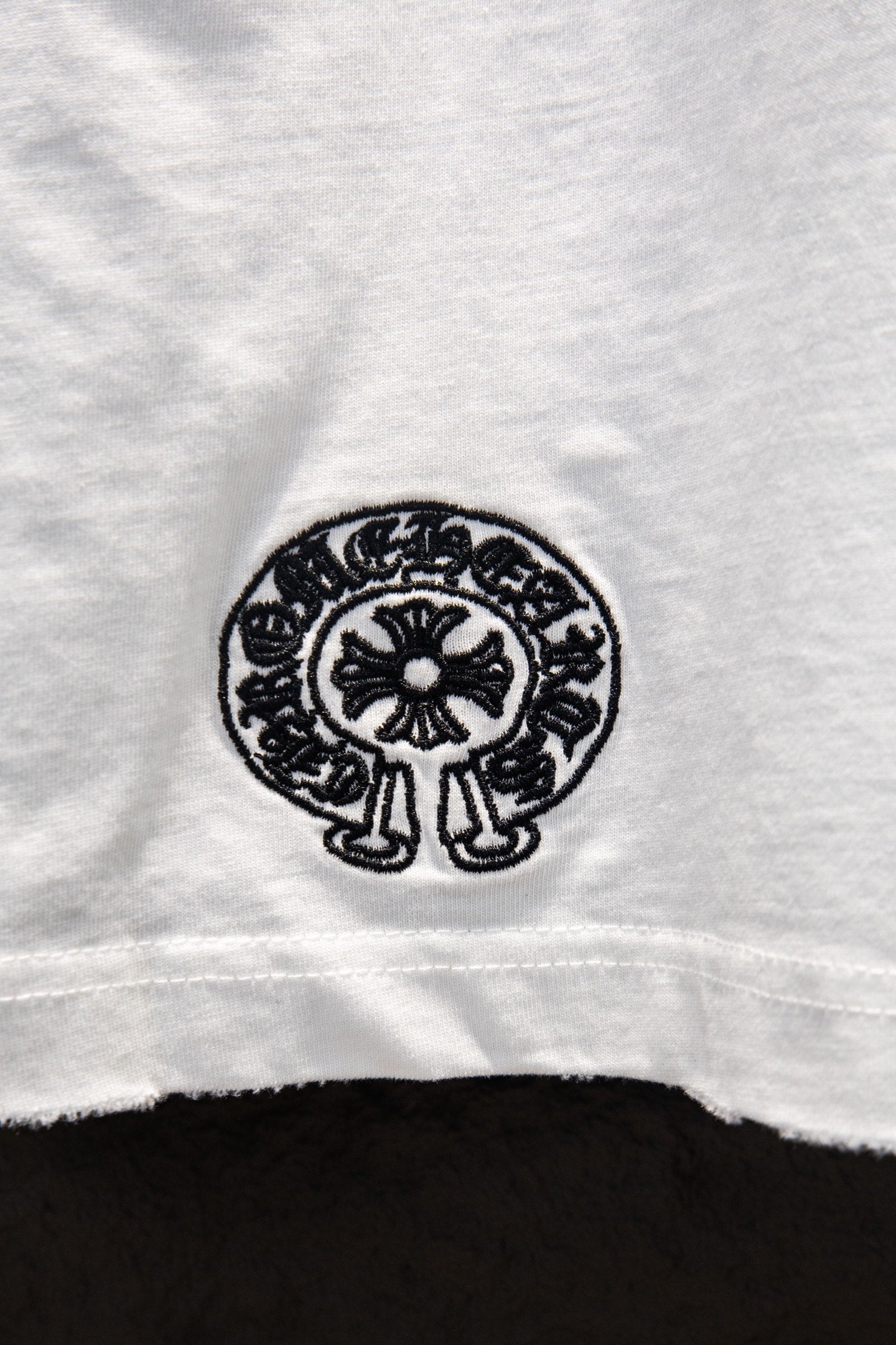 White T-shirt with small black circular emblem at lower hem.