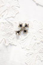 Embroidered floral cross ornament with black and gold beaded accents on white fabric