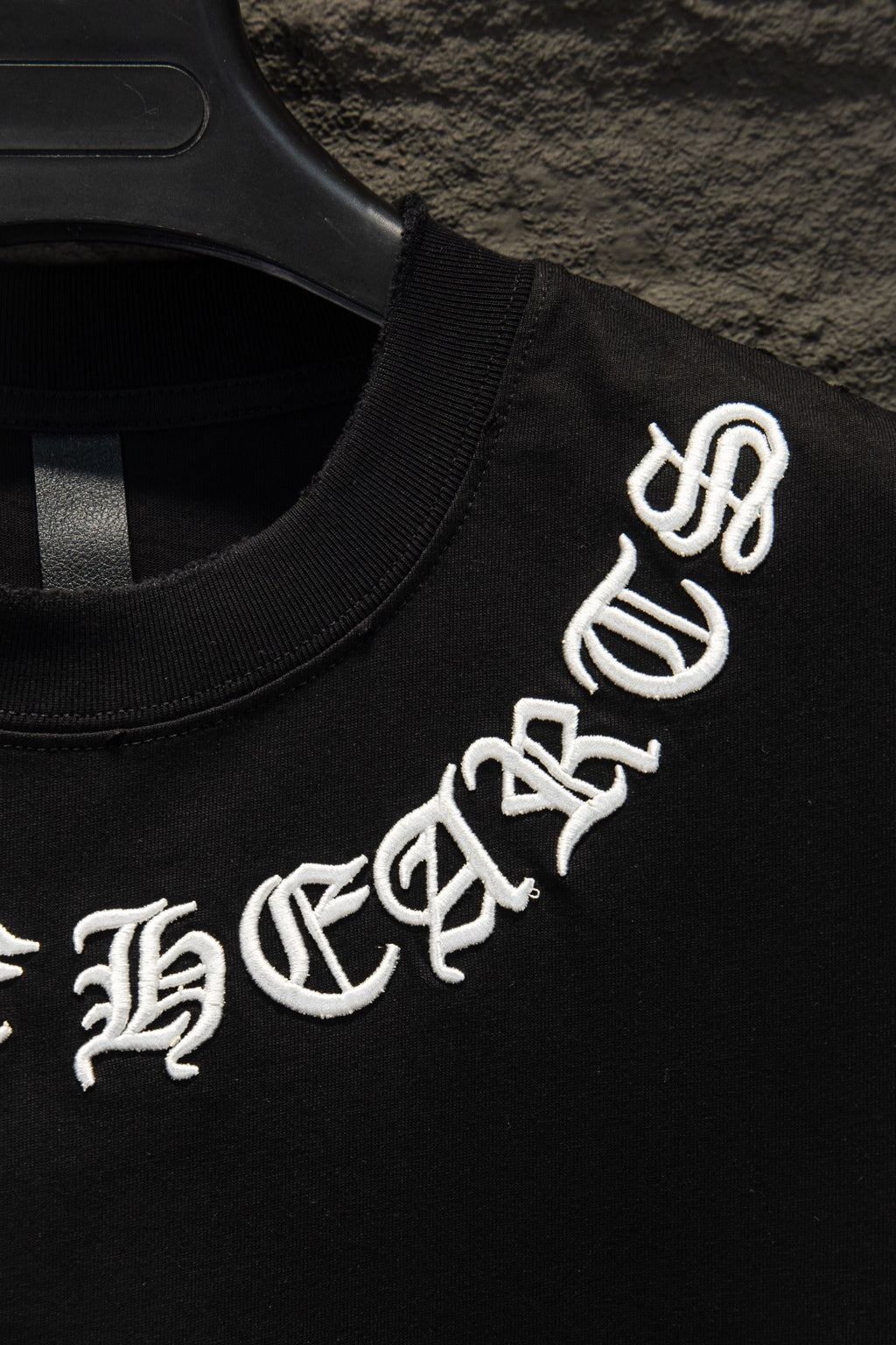 Black T-shirt with white logo graphic text on sleeve, on hanger