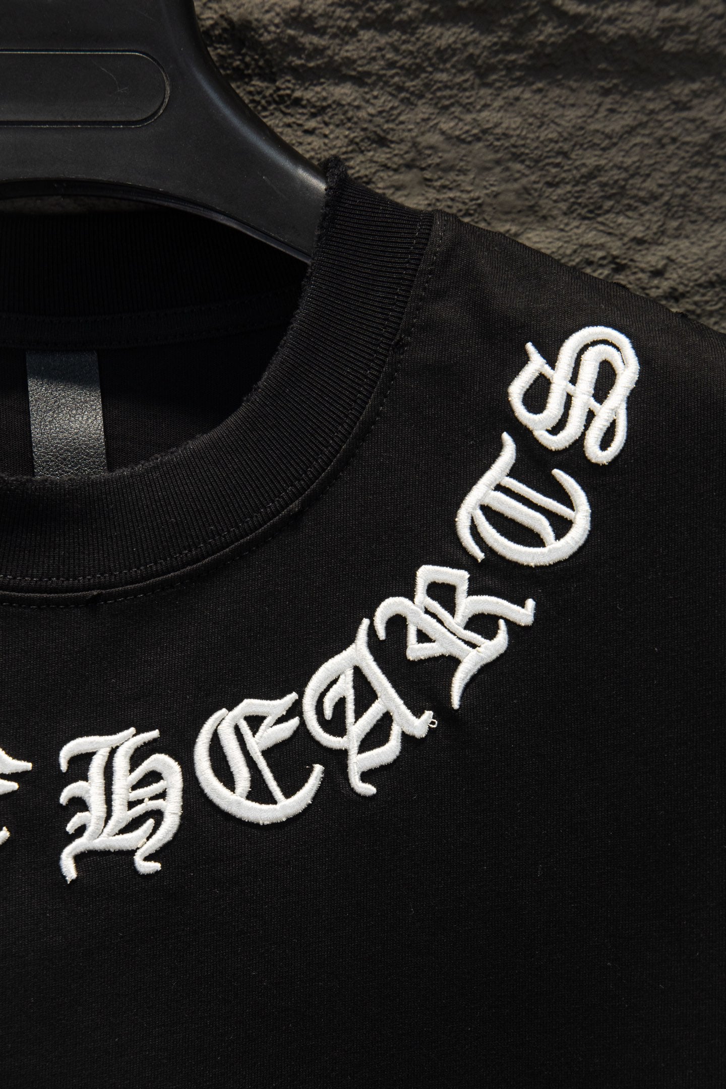 Black T-shirt with white logo graphic text on sleeve, on hanger