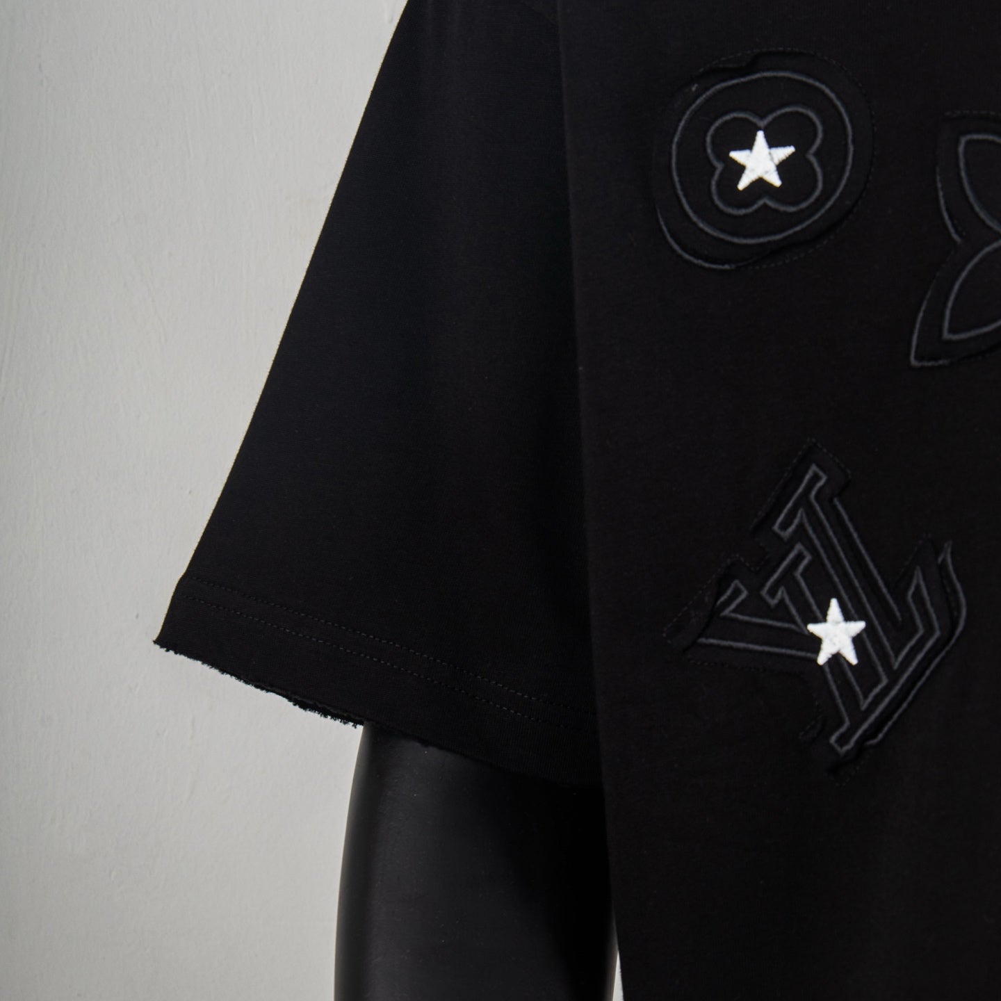 Black T-shirt sleeve with tonal LV logo and star emblem applique