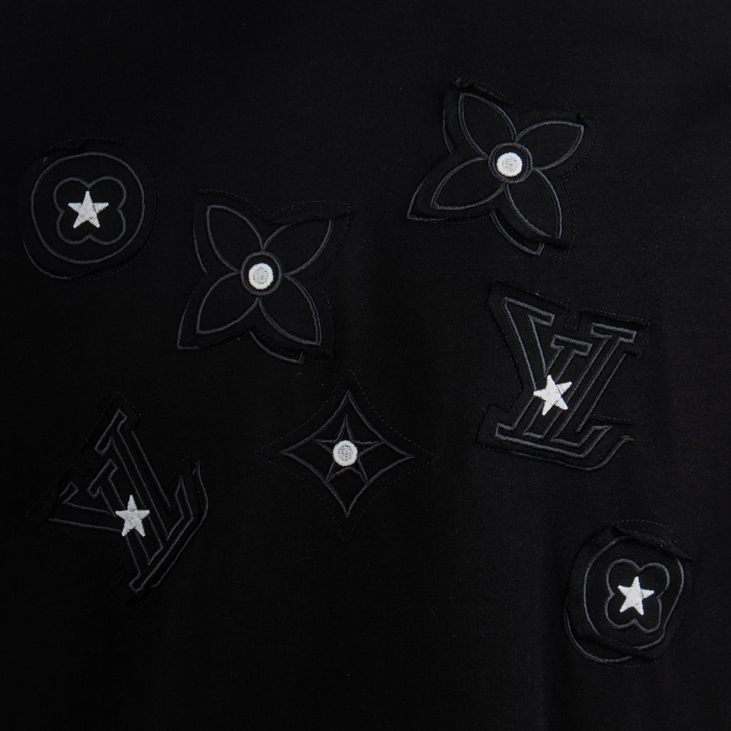 Black T-shirt with dark-on-black flower, star, and LV-style emblems