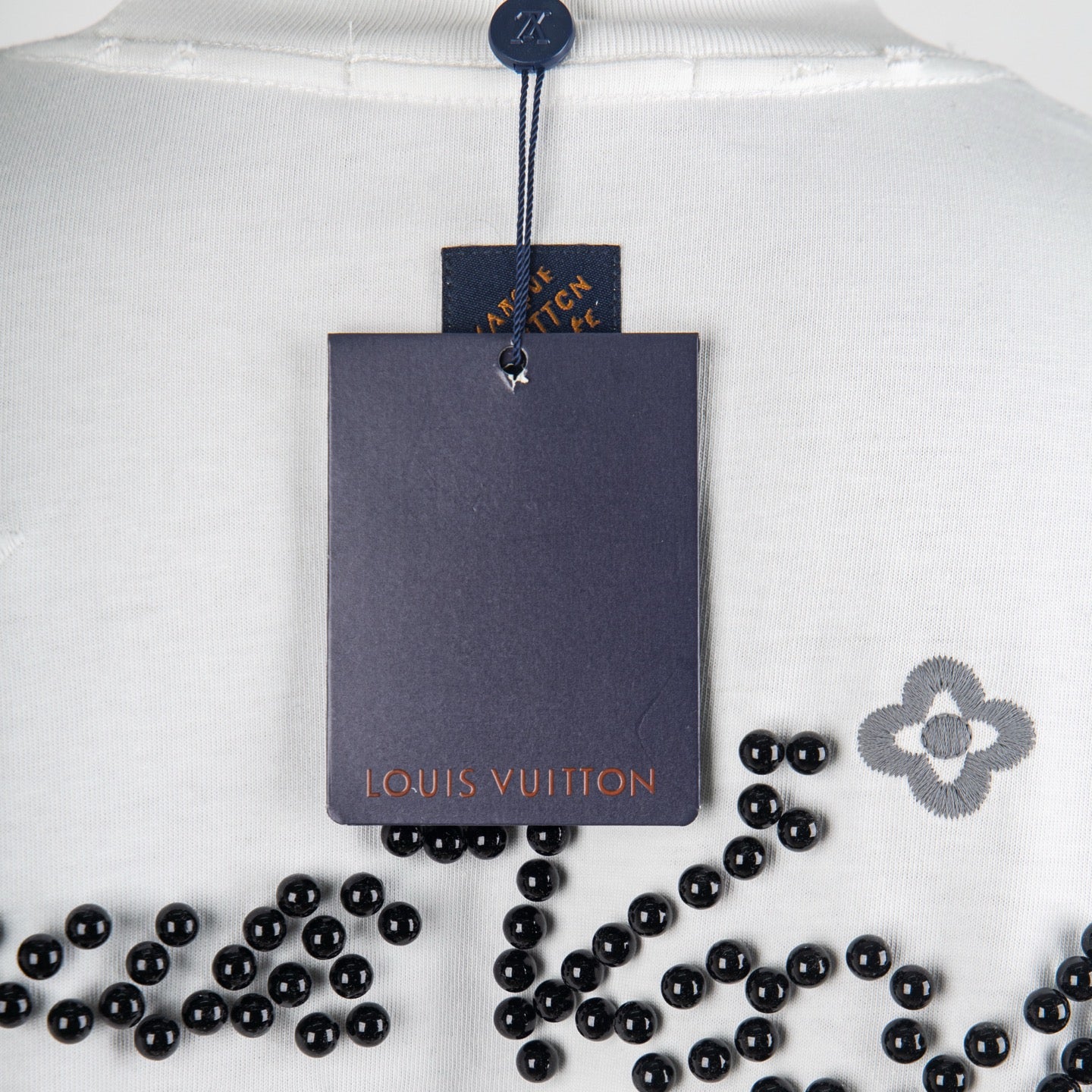 Louis Vuitton white T-shirt close-up with neck hang tag and black beaded motif
