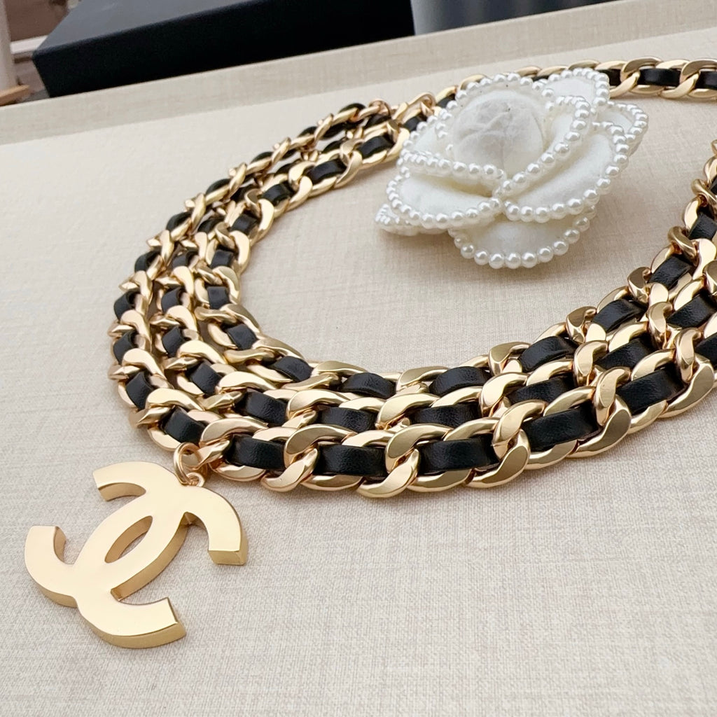 Chanel belt with gold-and-black chain links, gold CC charm, and white flower accent