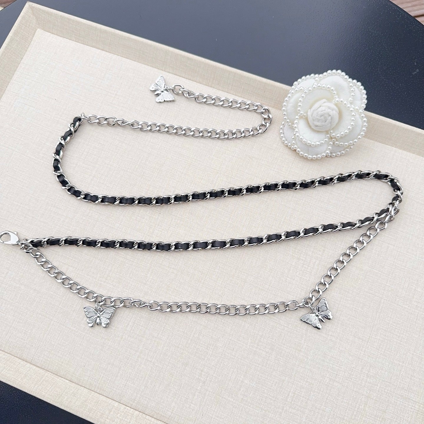 Multi-strand chain belt with silver and dark links, butterfly charms, and a white flower clasp.