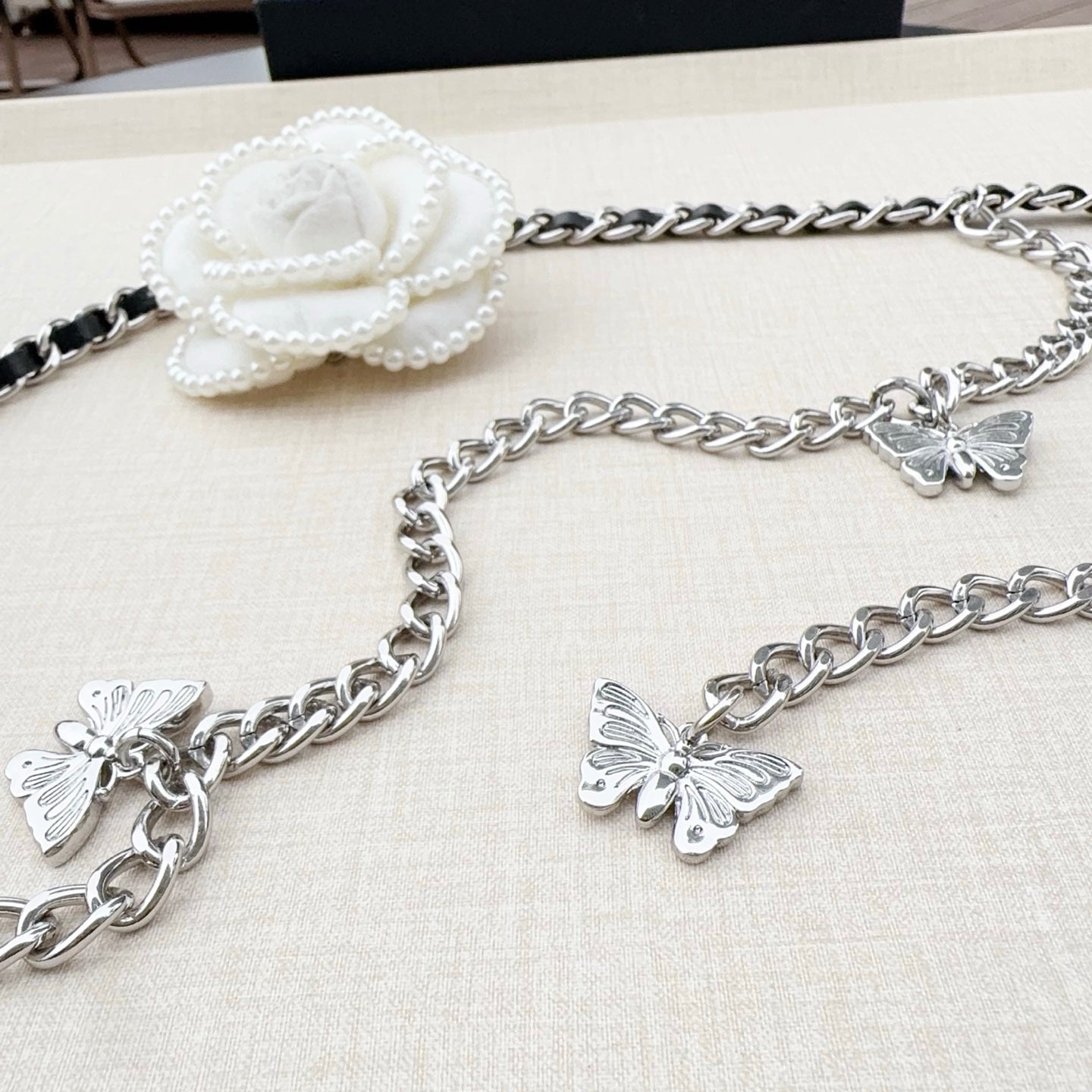 Silver chain belt with butterfly charms and a white flower clasp at the top.