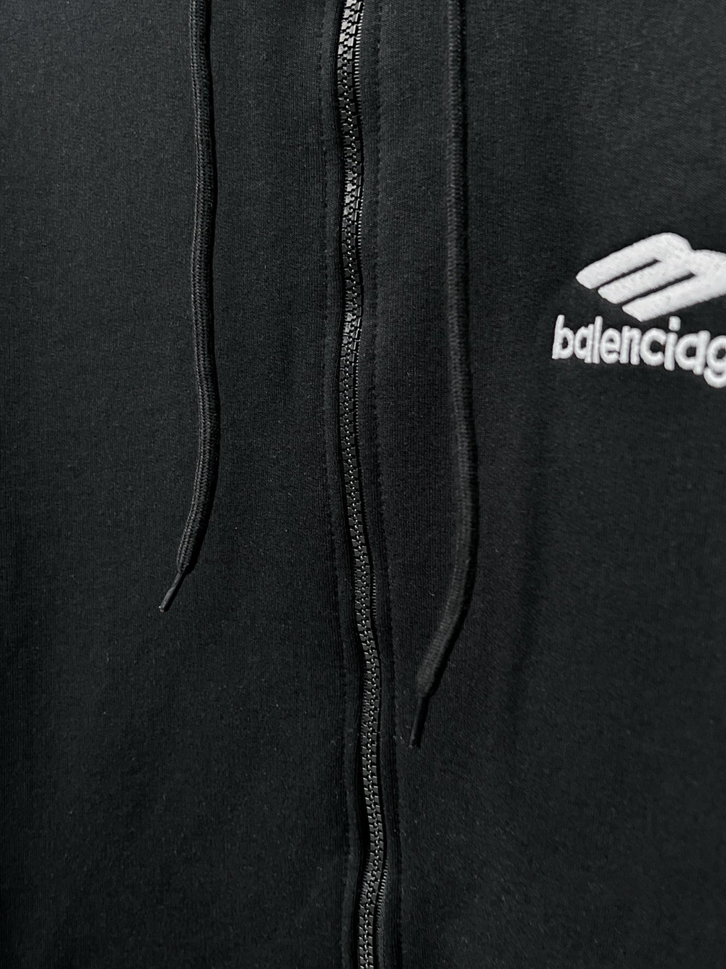 Balenciaga black zip hoodie close-up: center zipper, hood strings, chest logo