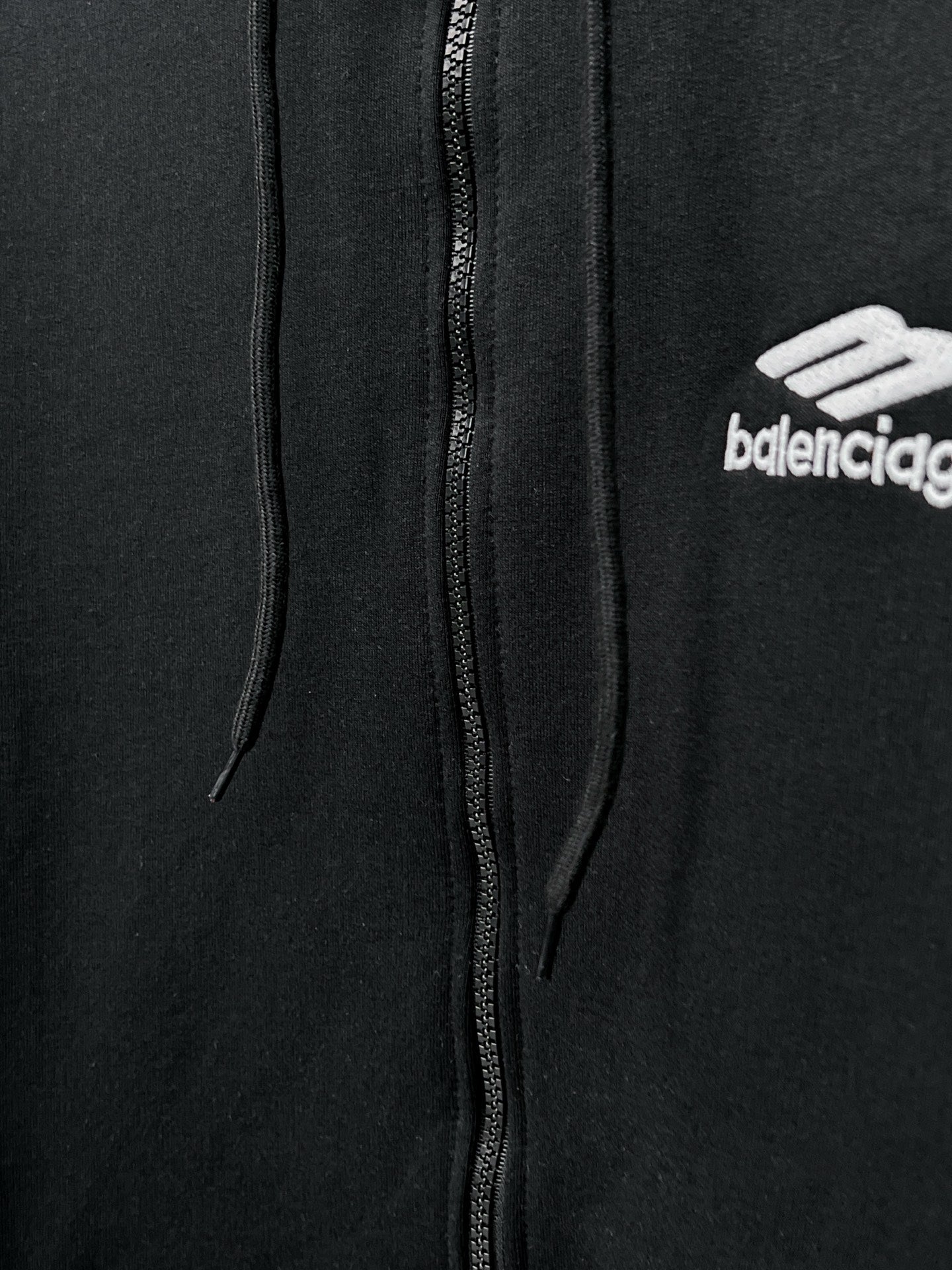 Balenciaga black zip hoodie close-up: center zipper, hood strings, chest logo