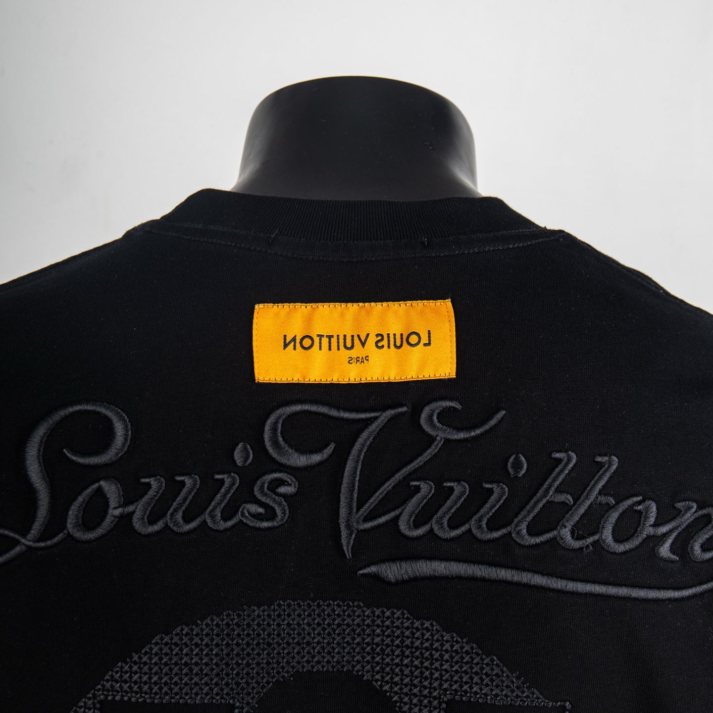 Black T-shirt back neckline with Louis Vuitton script and yellow label.