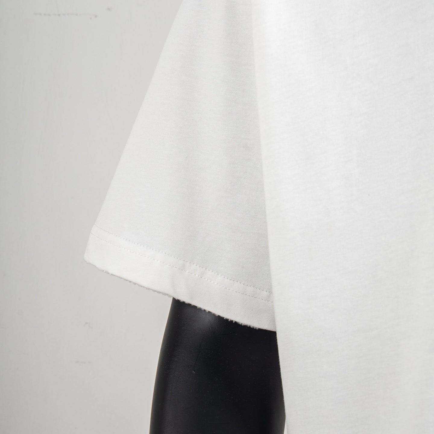 White T-shirt hem and side seam detail over a dark mannequin arm