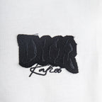Black embroidered logo patch on white T-shirt front