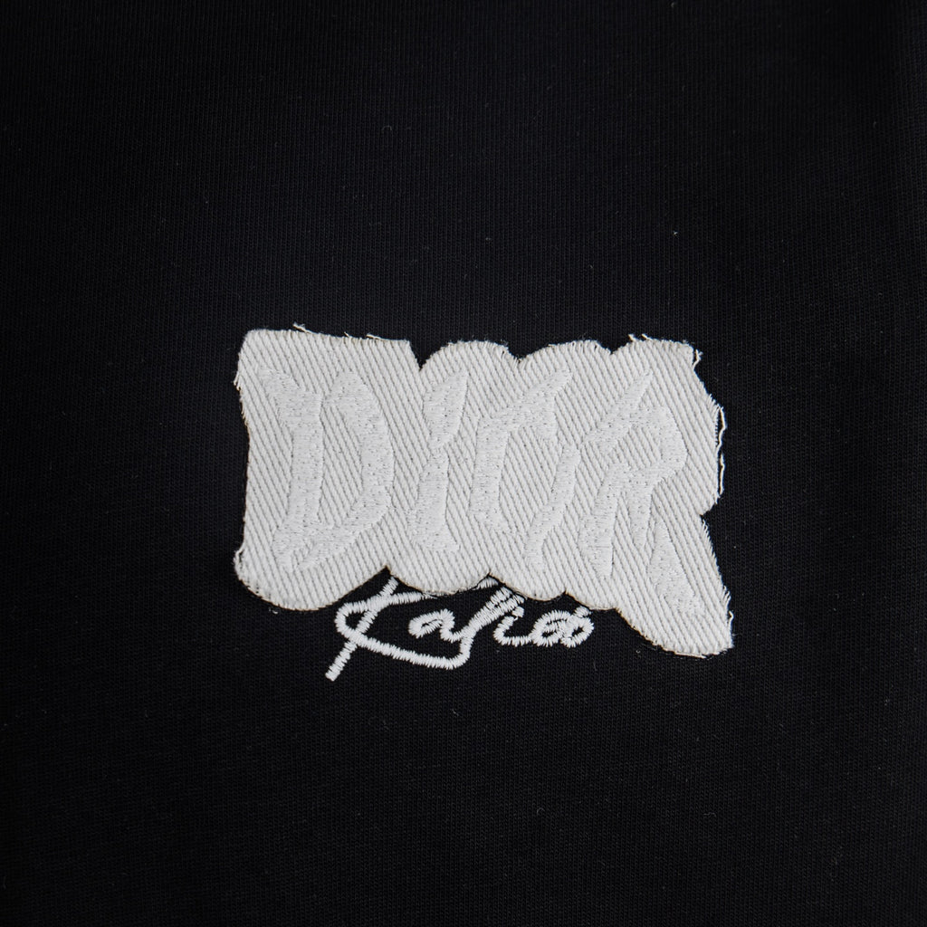 White embroidered Dior logo patch on black T-shirt chest.