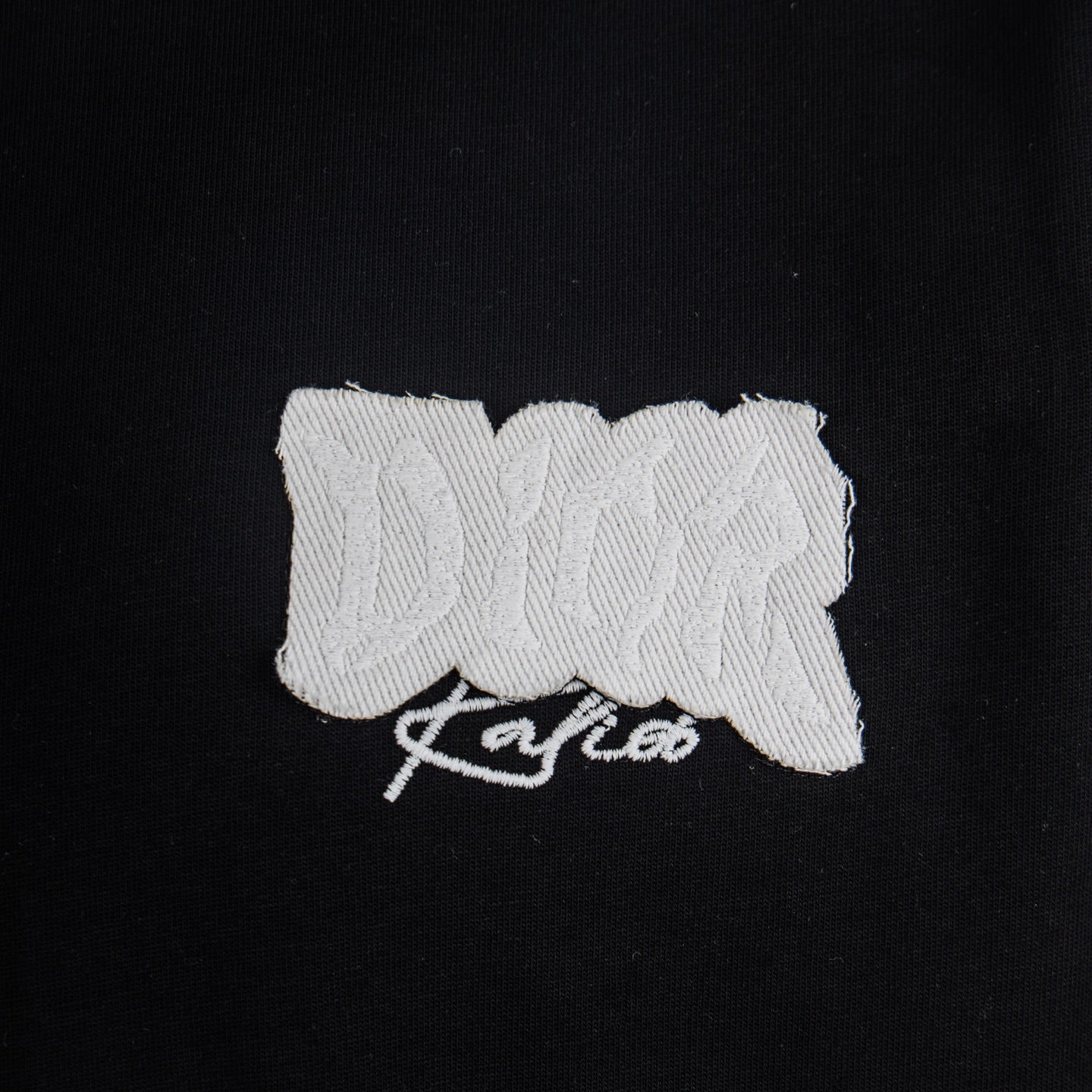 White embroidered Dior logo patch on black T-shirt chest.