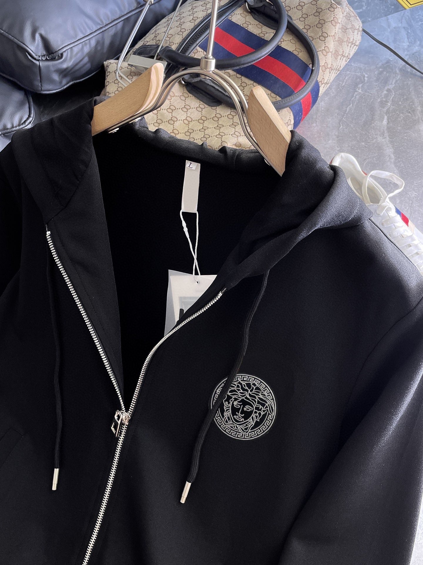 Black hooded jacket detail with zipper, drawstring cords, and circular logo patch